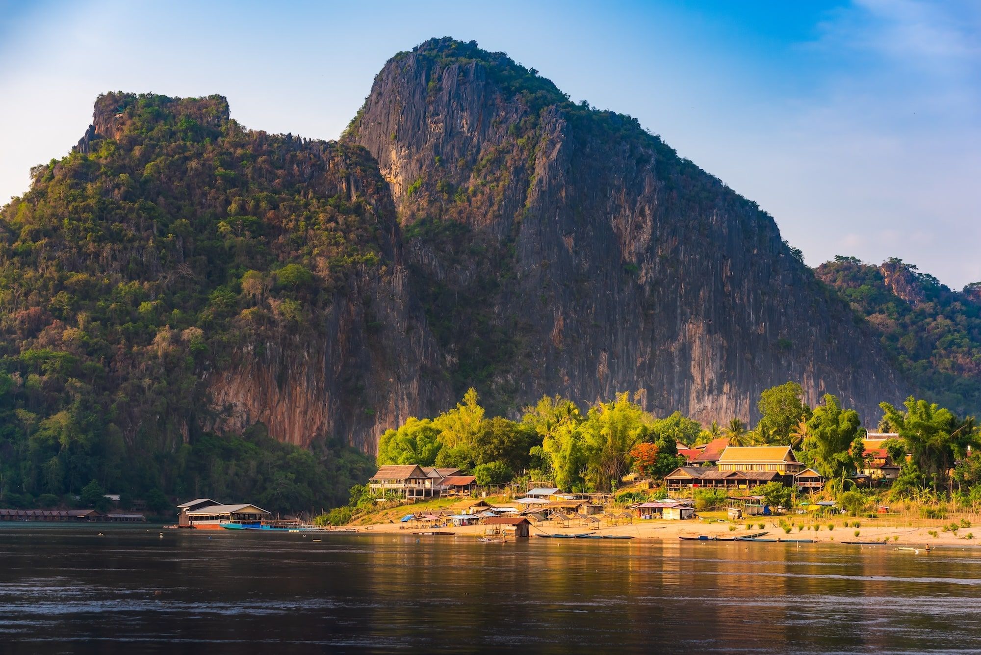 A village below wooded limestone cliffs on the bank of the Mekong