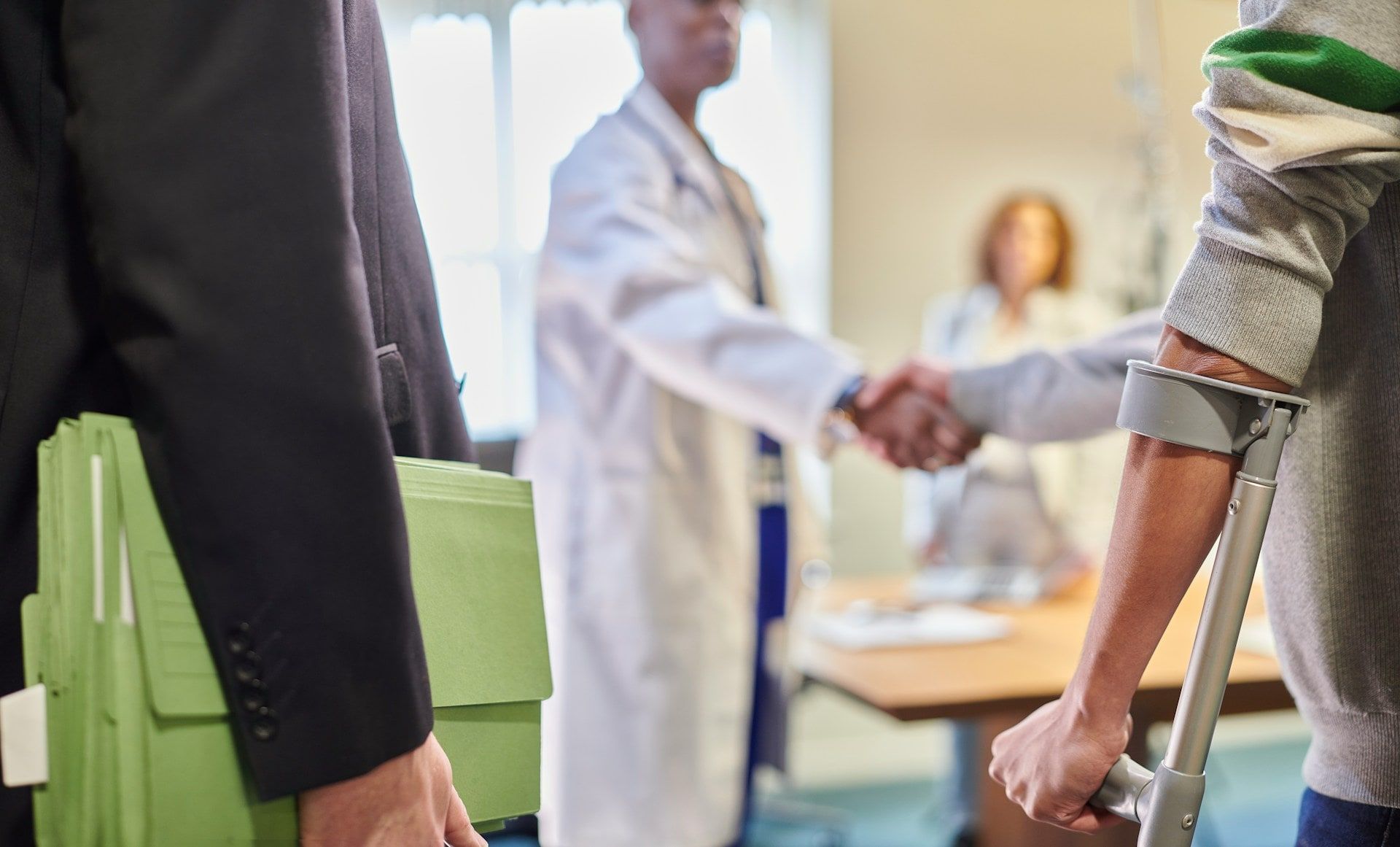 Un médecin serre la main d'un patient en béquilles, au premier plan un dossier vert sous le bras d'un homme en costume