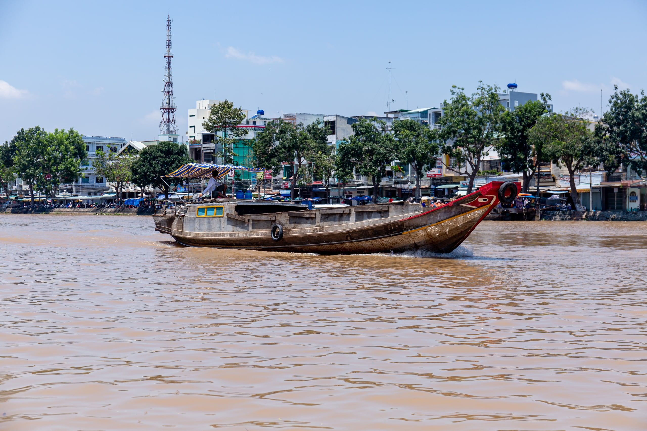 Un bateau de bois chargé descend la rivière devant les quais de Bến Tre