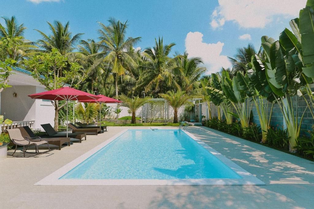 La piscine de La Villa de Coco, transats et parasols rouges, entourée de cocotiers et de bananiers