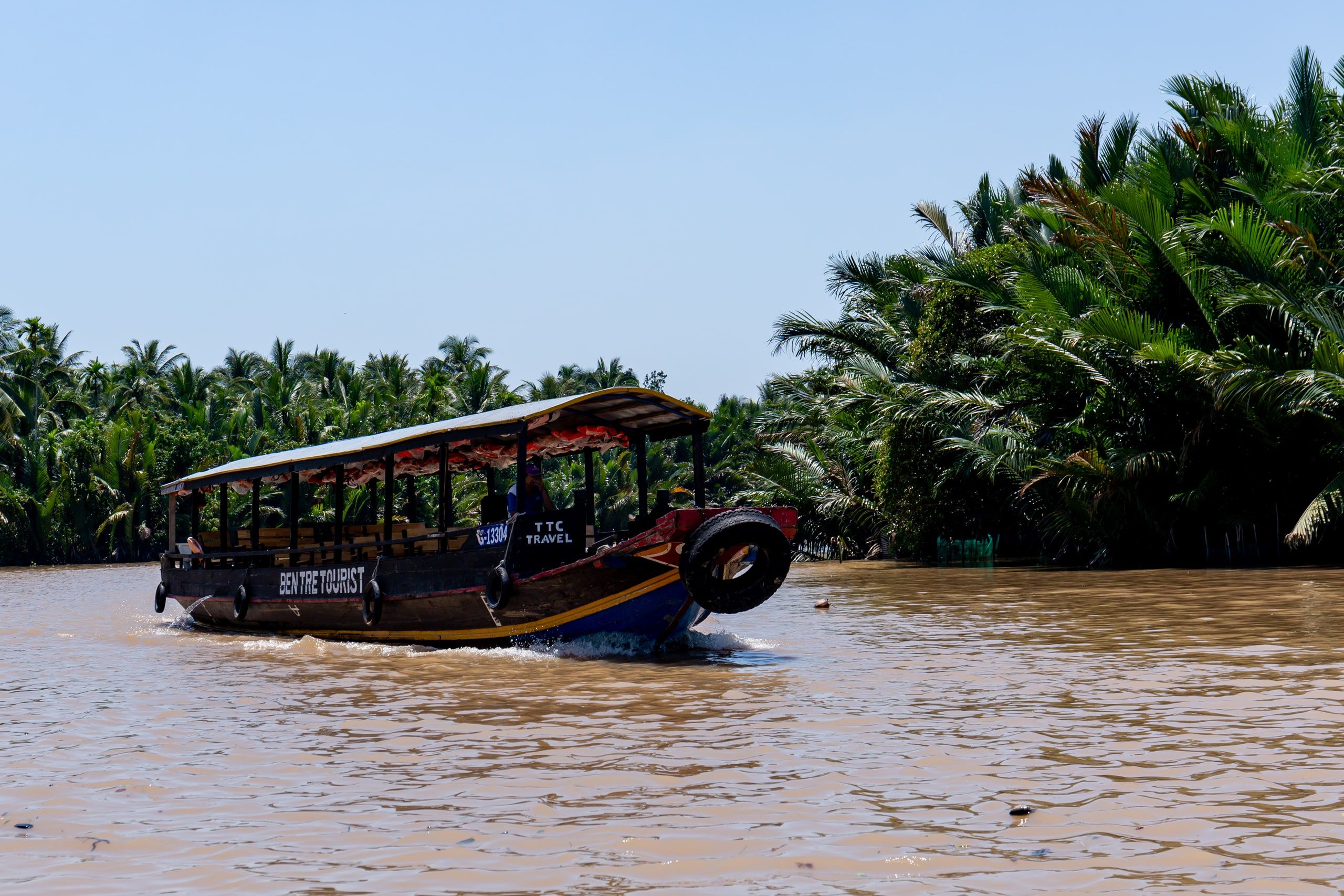 Un bateau de touristes passe devant les palmiers nipa, sur une rivière de Bến Tre
