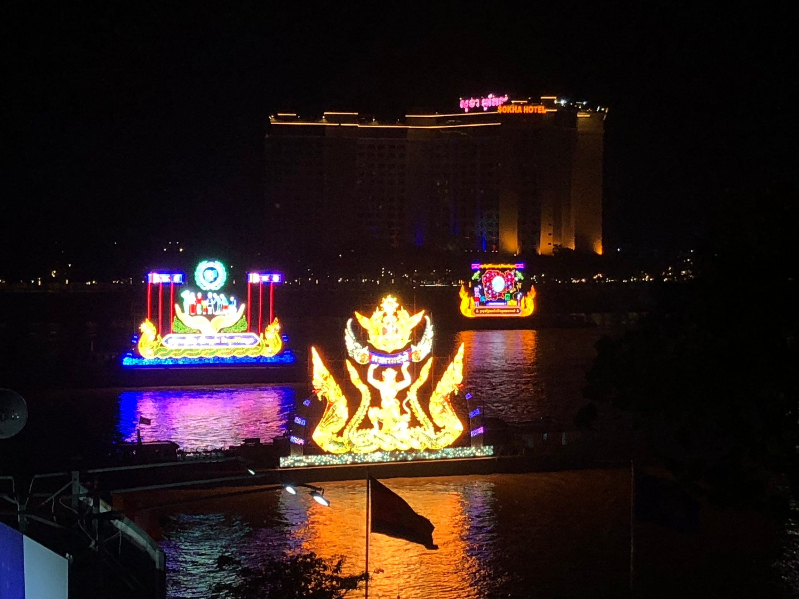 Bateaux illuminés du Loy Pratip la nuit sur le Tonlé Sap, l'un en forme de couronne dorée, devant un hôtel éclairé