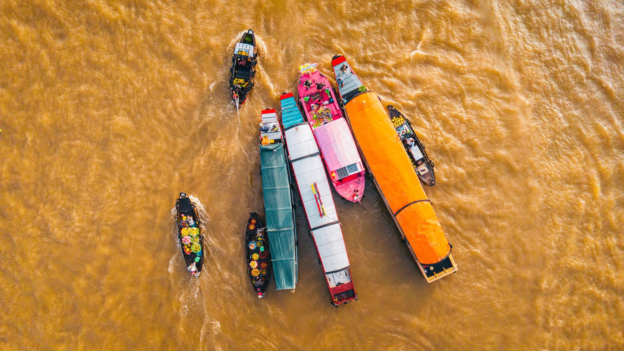 Cai Rang floating market from above: merchant boats with brightly painted hulls moored side by side on the brown water of the Can Tho River
