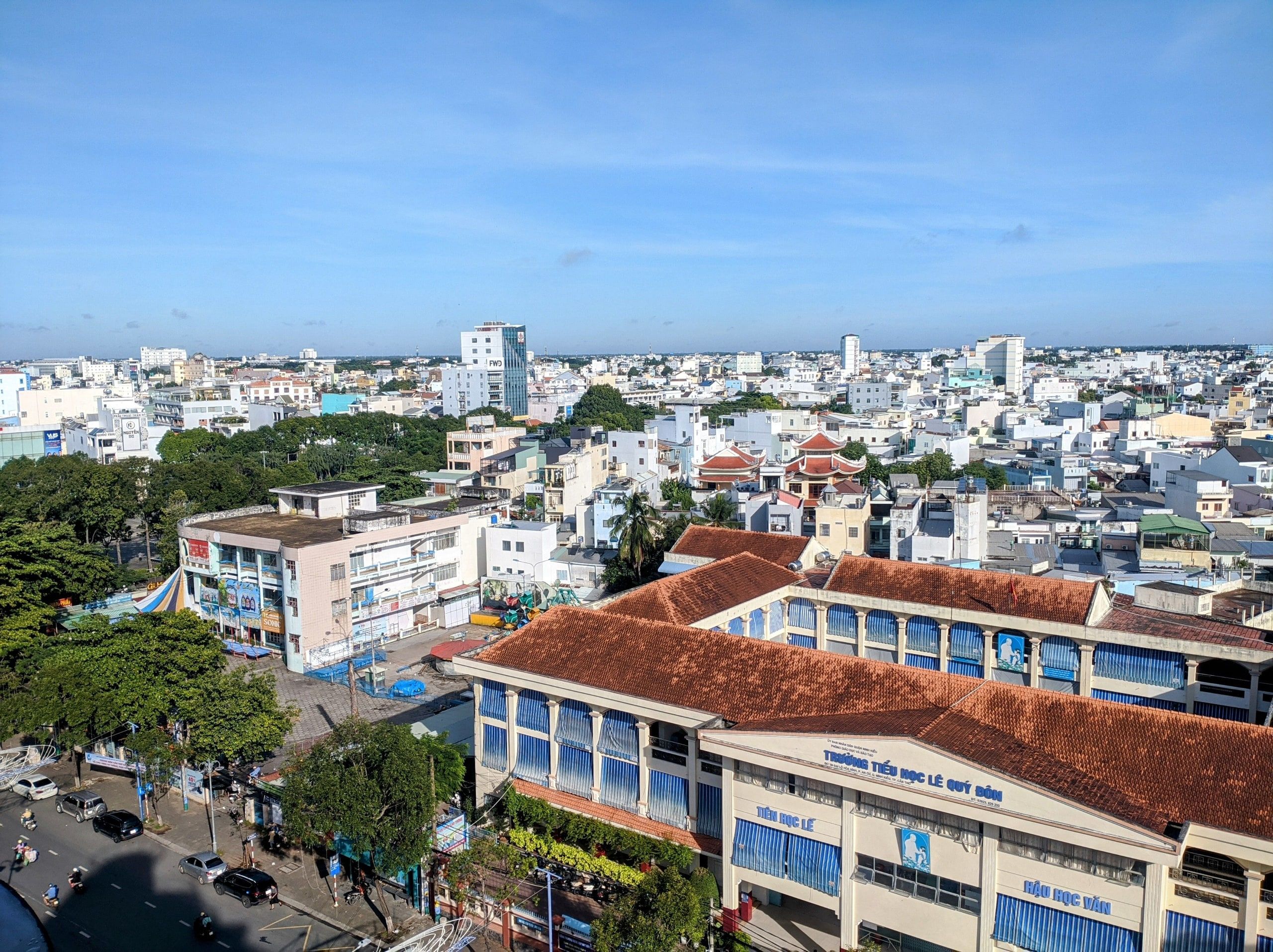 Can Tho from above: low-rise buildings, tiled roofs and a tree-lined street under a blue sky