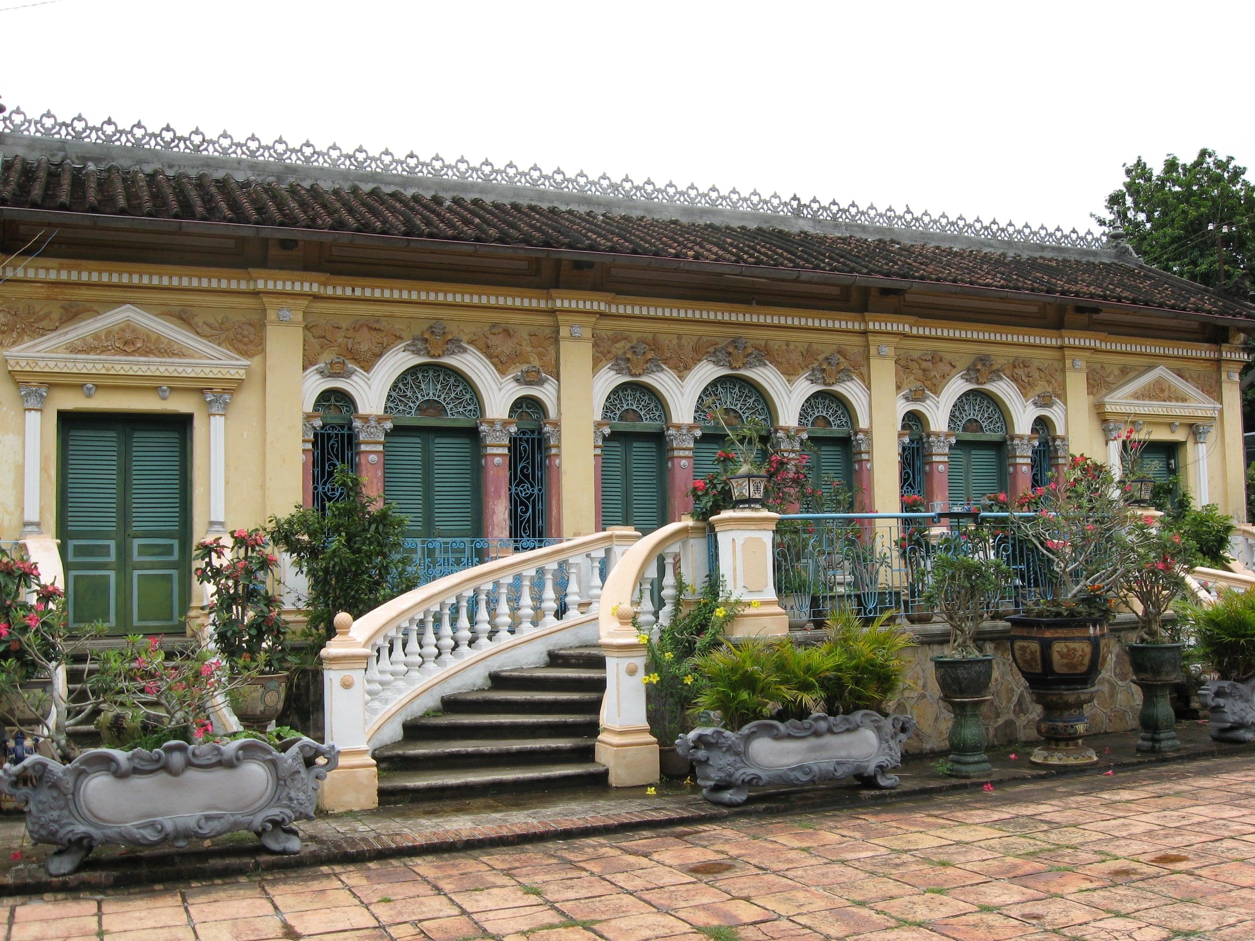 The facade of Binh Thuy Ancient House, with its arches and double staircase among bonsai planters