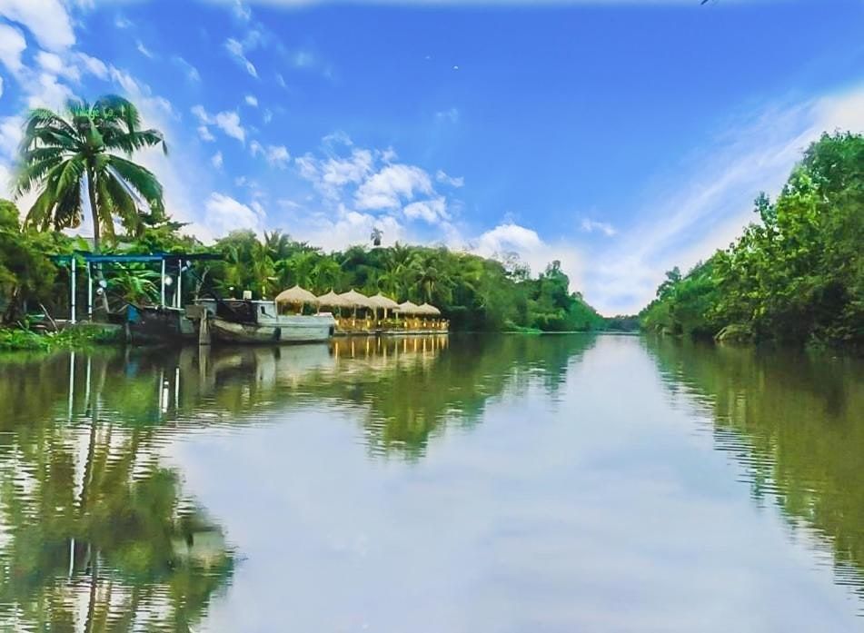 The river beside Bamboo Eco Village, lined with coconut palms, with the property's jetties and thatched huts on the bank