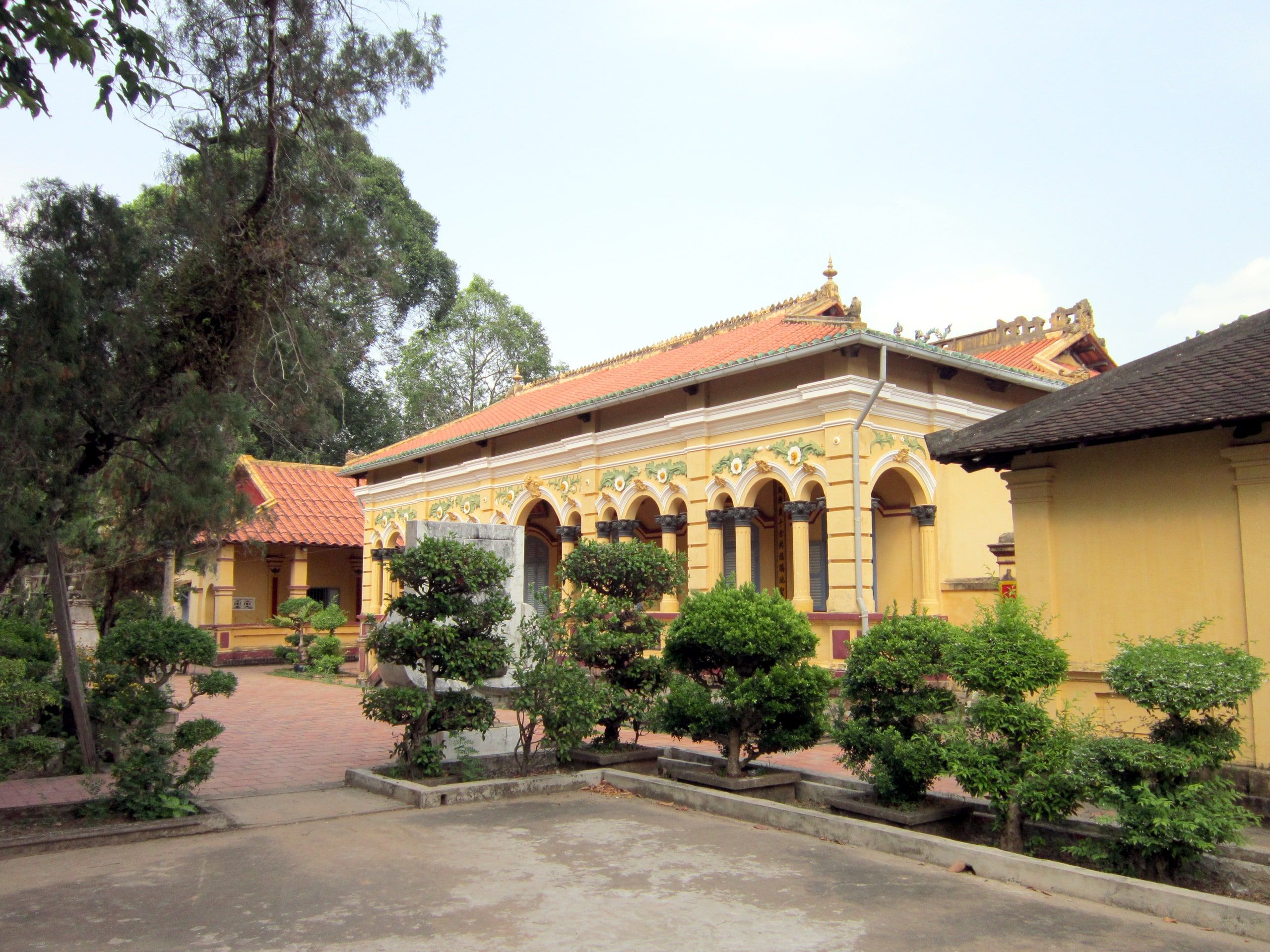 Nam Nha Pagoda in Binh Thuy: a yellow building with arches and a tiled roof, behind a courtyard of clipped shrubs