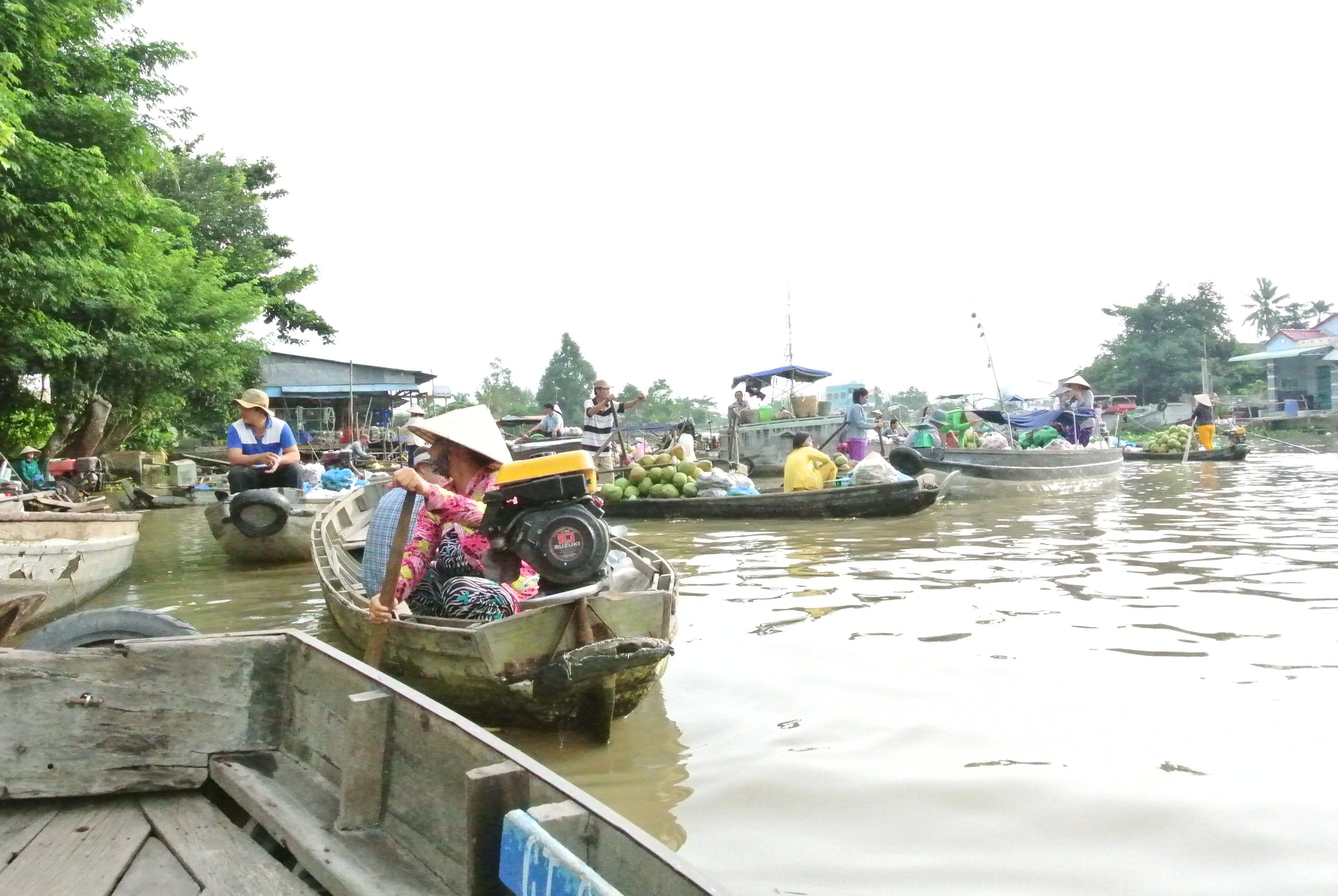 A vendor in a conical hat on her boat at the Phong Dien floating market, among other boats loaded with fruit
