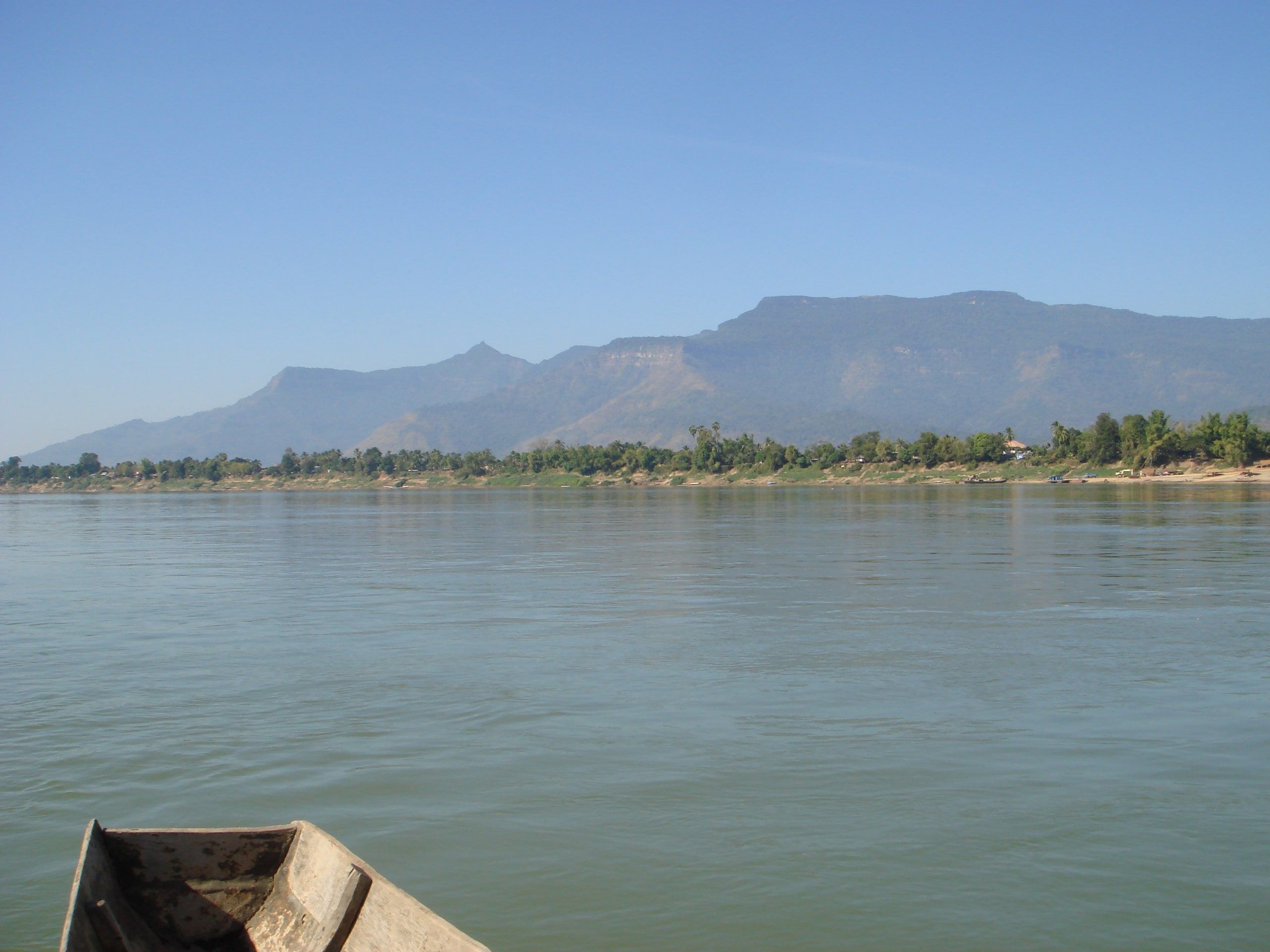 Champasak seen from the Mekong, a boat in the foreground and mountains behind the village
