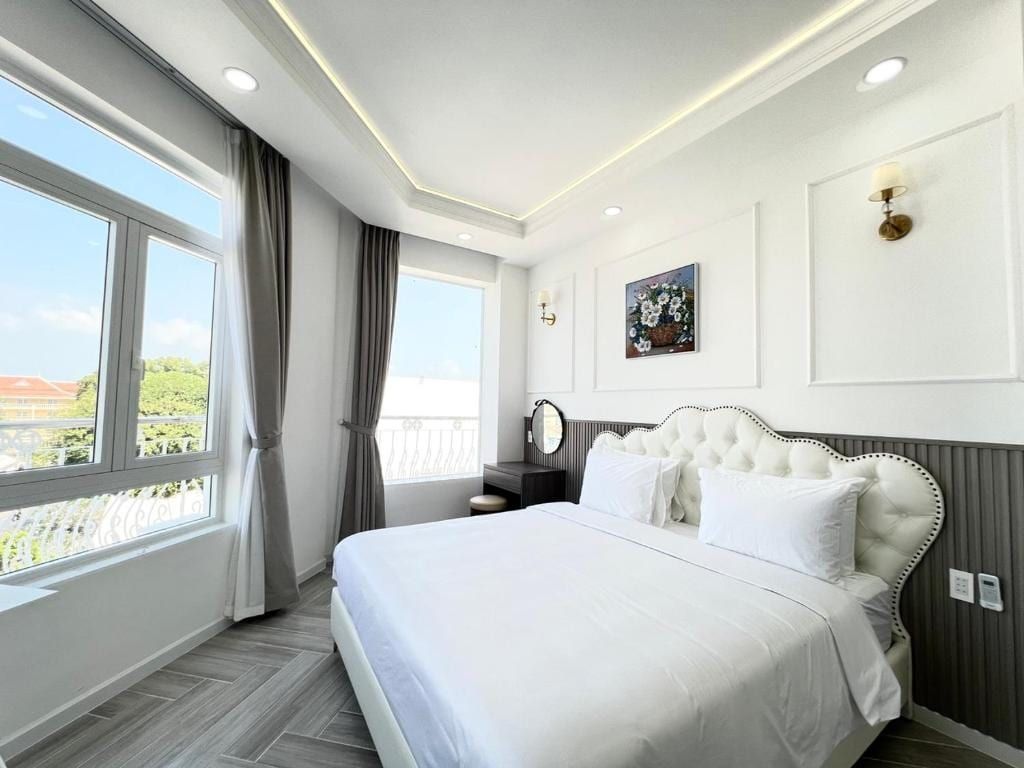Une chambre blanche du Paris Hotel, lit capitonné et grandes fenêtres