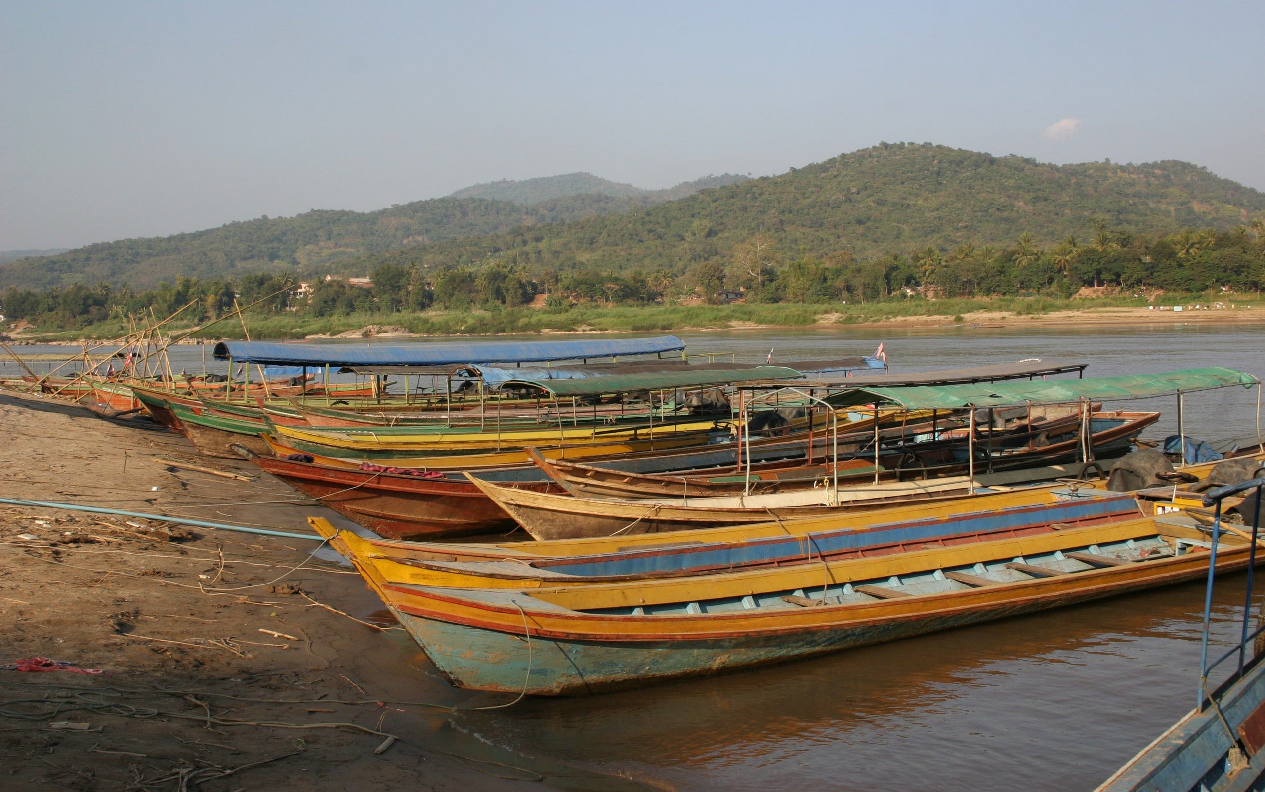 Des bateaux à longue queue amarrés sur la berge du Mékong à Chiang Khong, la rive laotienne en face