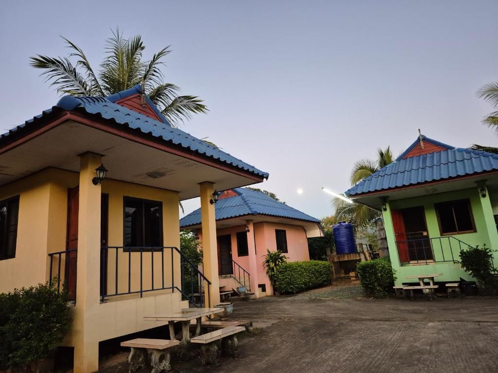 Three yellow, pink and green bungalows with blue roofs at Panna Kalong, at dusk