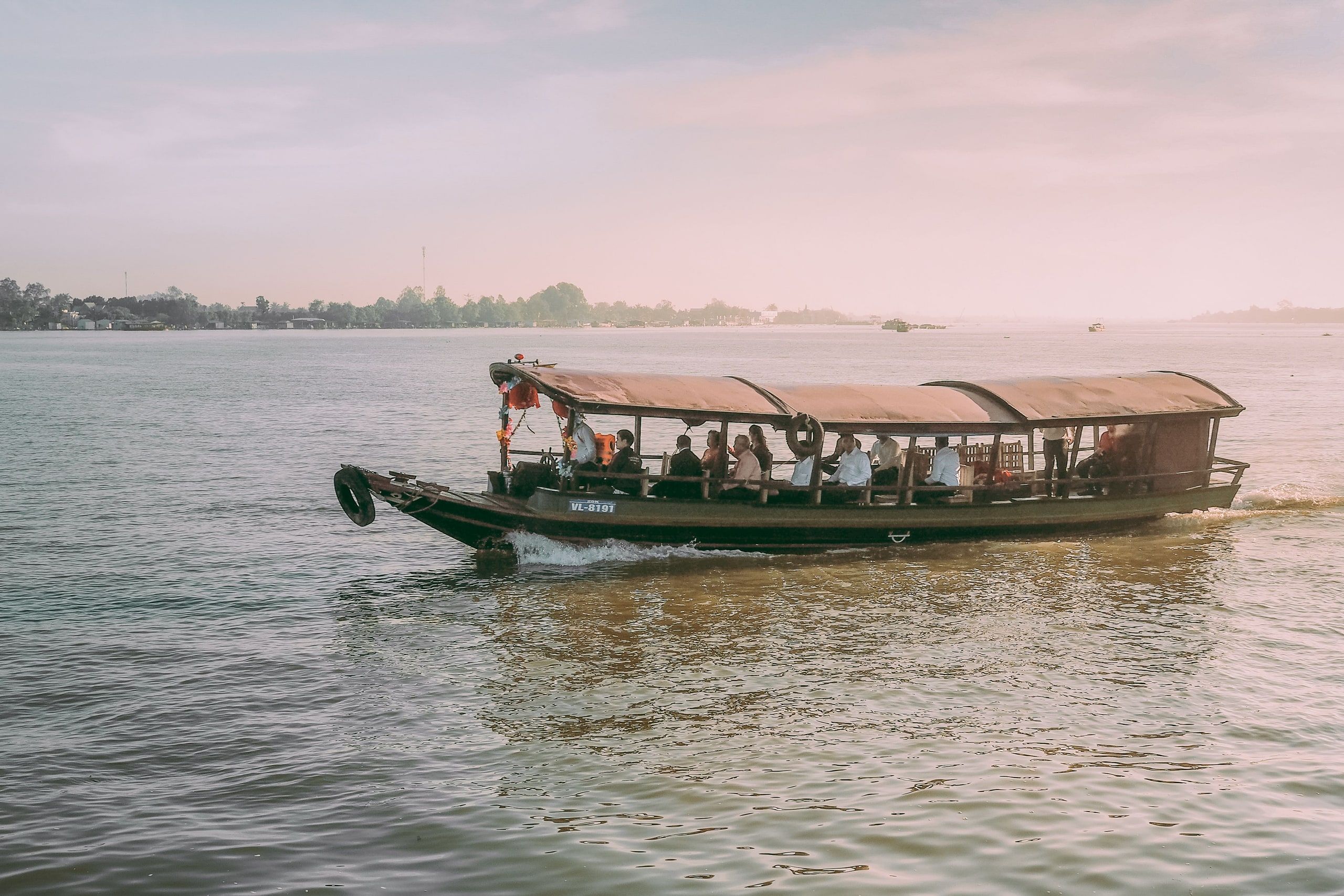 A traditional wooden boat carrying passengers on the Mekong at Vinh Long, Vietnam, at sunset