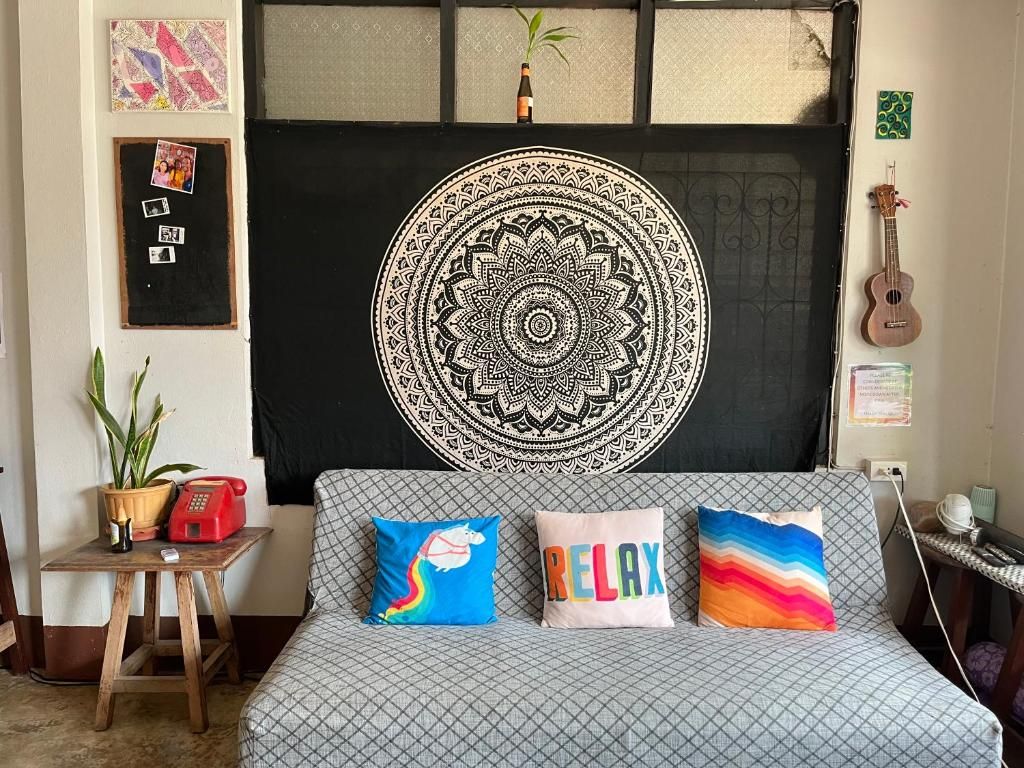 The lounge at Little Hostel, a sofa with colorful cushions in front of a mandala hanging, a ukulele on the wall