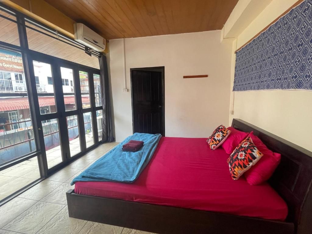 A room at Over the Moon Hostel, a bed with red sheets and glass doors onto the street