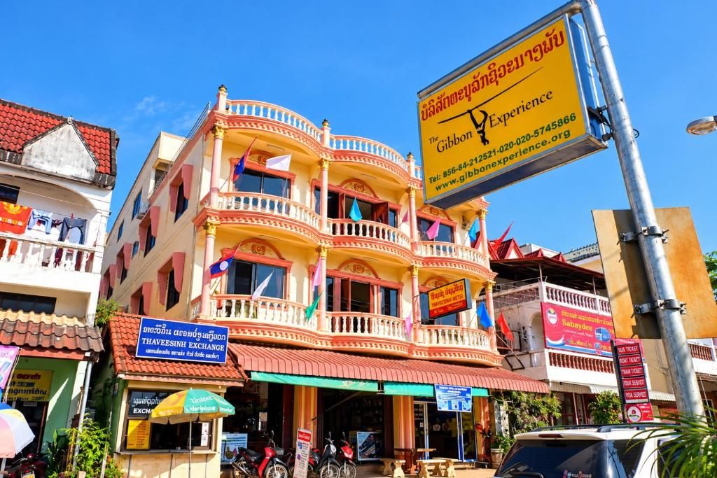 The pink and cream front of Thaveesinh Hotel with its balustraded balconies, next to the yellow Gibbon Experience sign