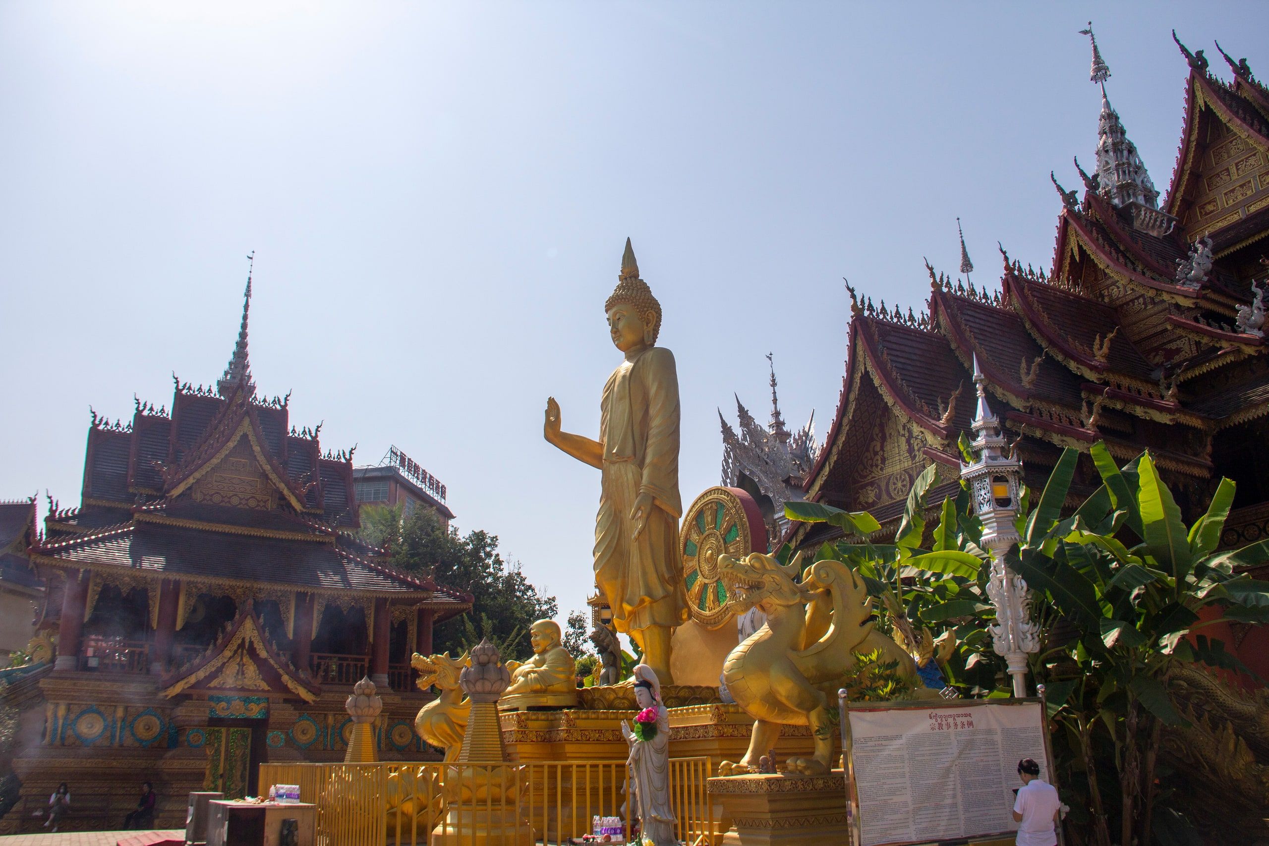 A standing golden Buddha before the roofs of a Dai temple in Manting Park
