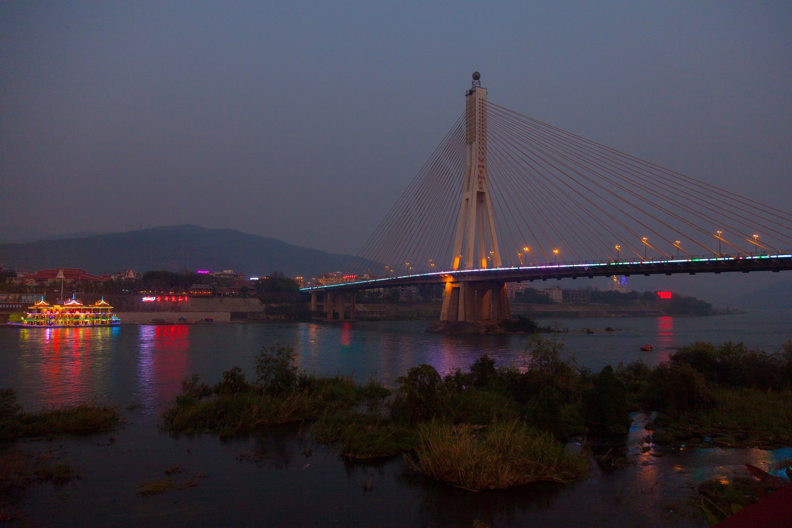 Jinghong's cable-stayed bridge at dusk, city lights on the river