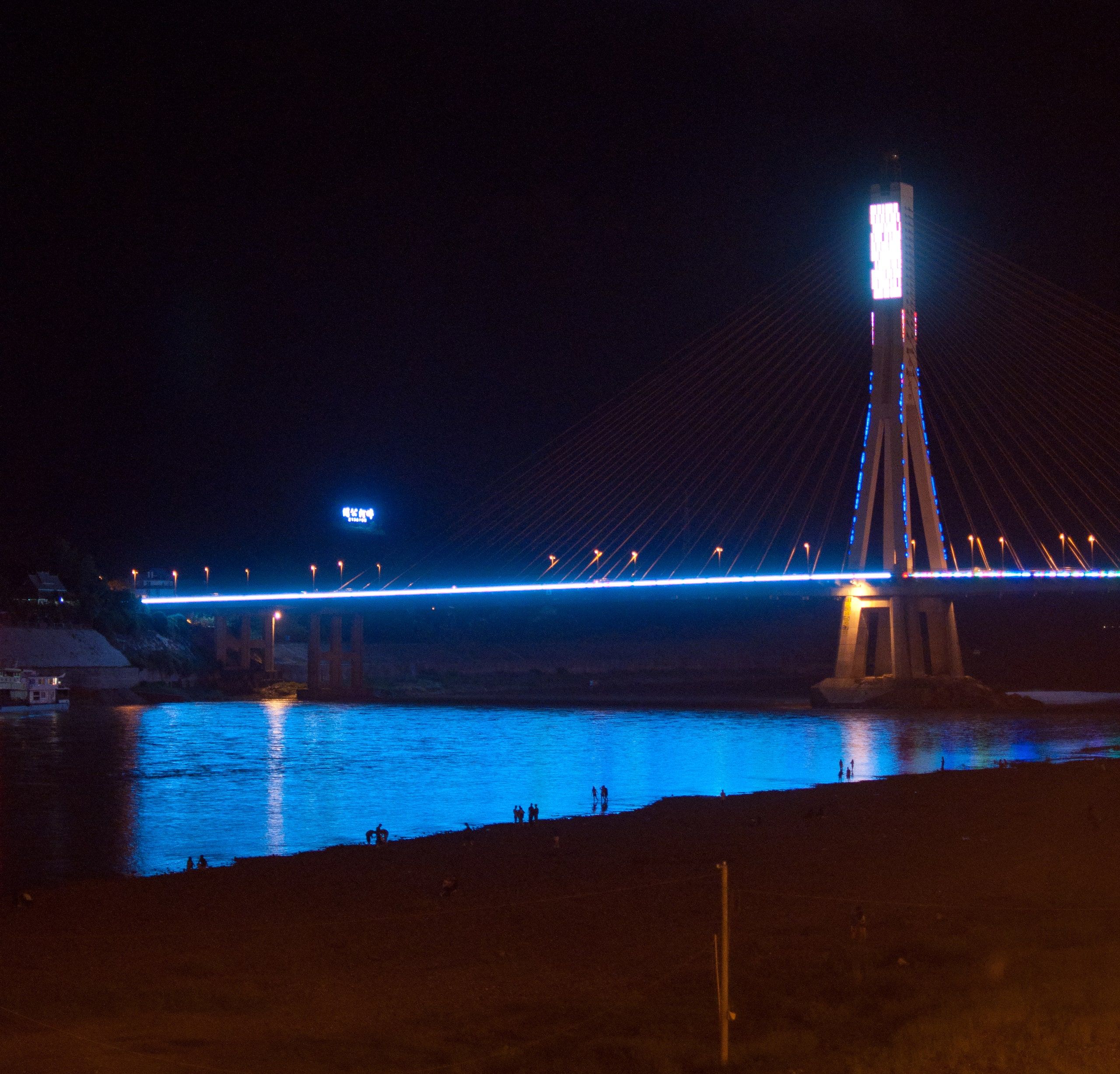 The Jinghong bridge lit up in blue at night above the Mekong