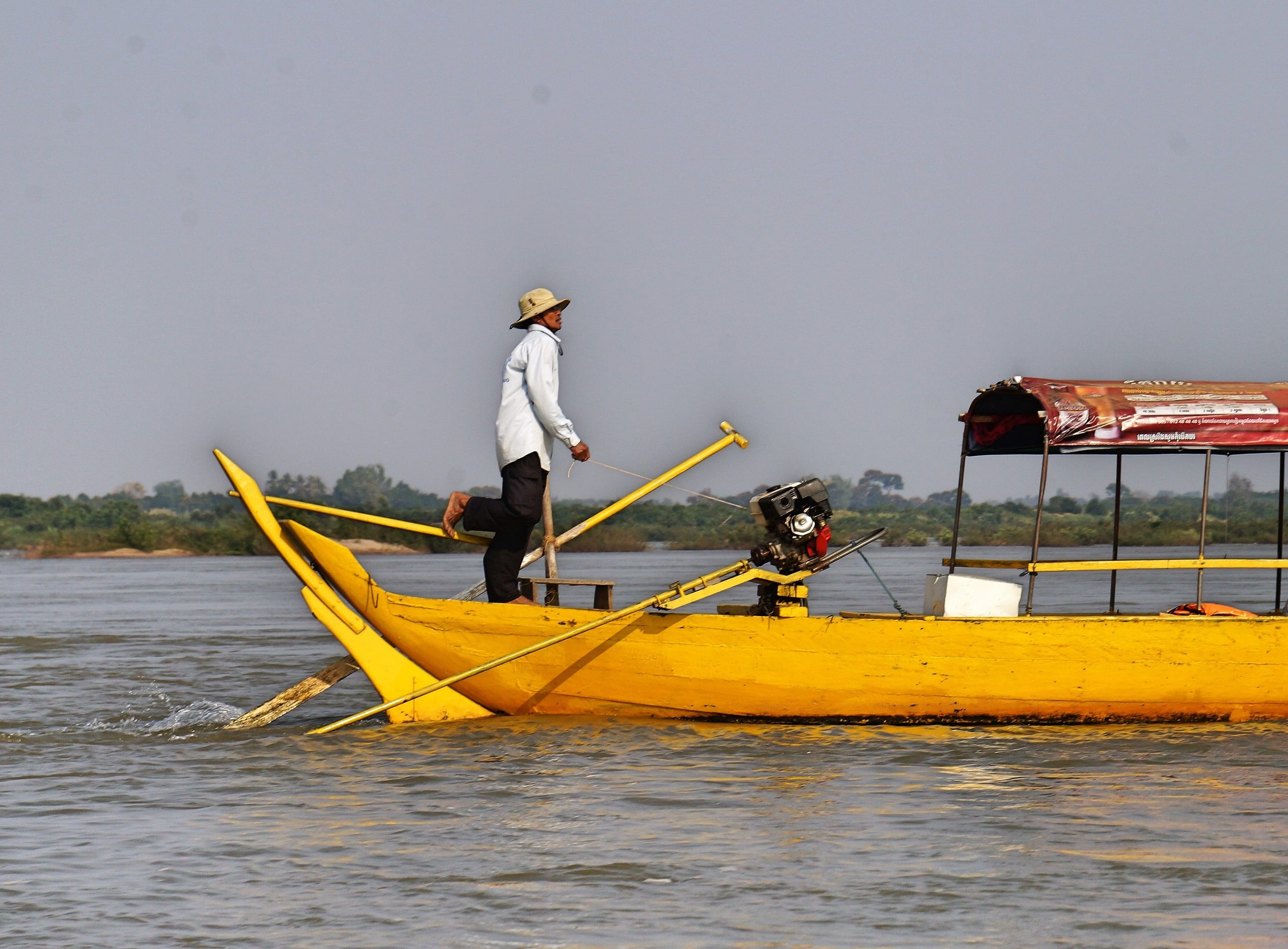 A boatman standing at the stern of his yellow boat at the Kampi pool