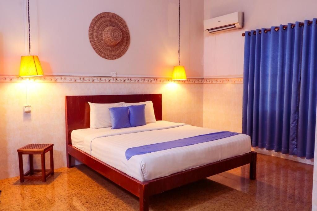 A room at Le Tonle, a double bed with blue cushions under two hanging lamps