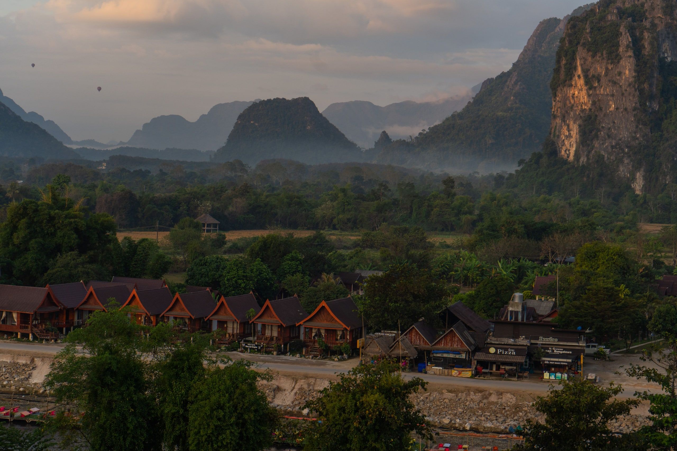 Des maisons de bois au pied des montagnes de Vang Vieng, dans la brume