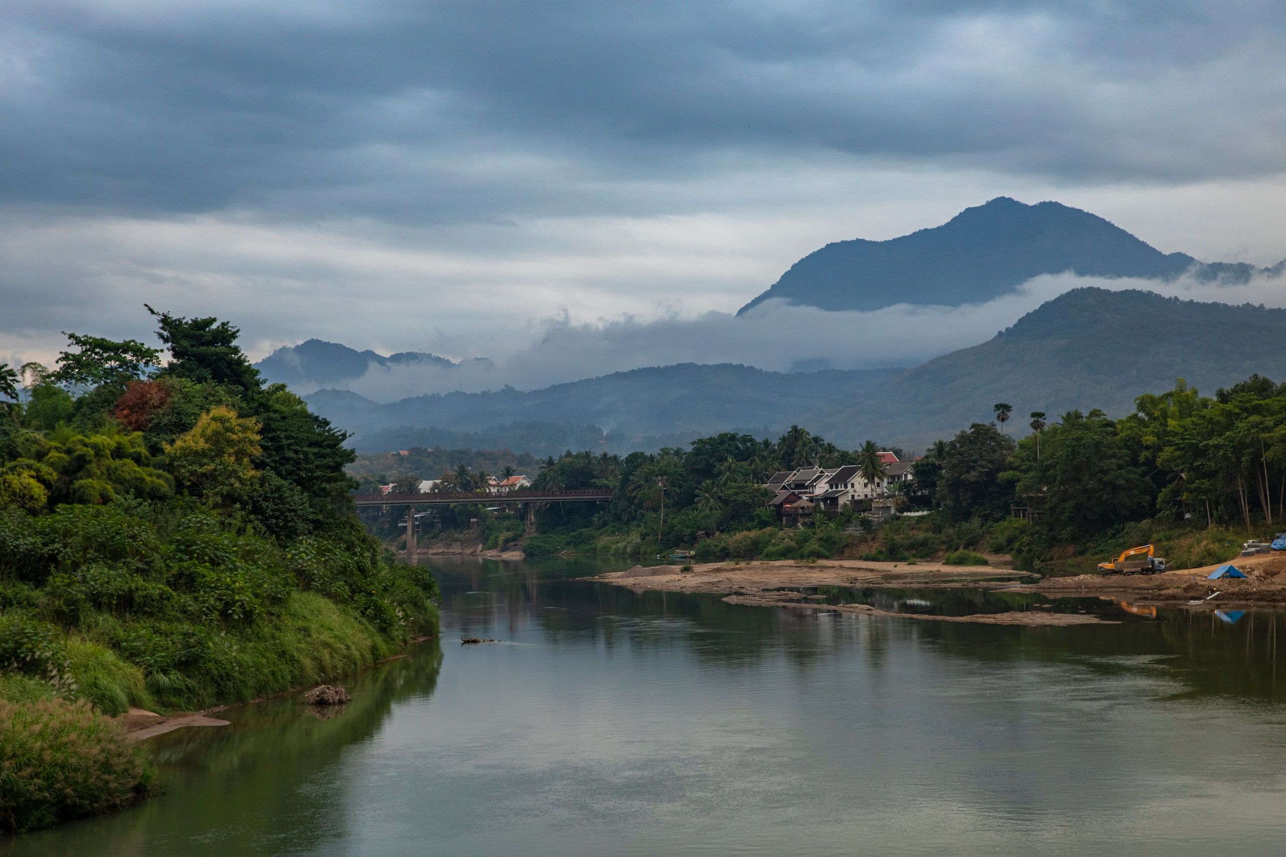 Une rivière entre les arbres, au pied de montagnes dans les nuages