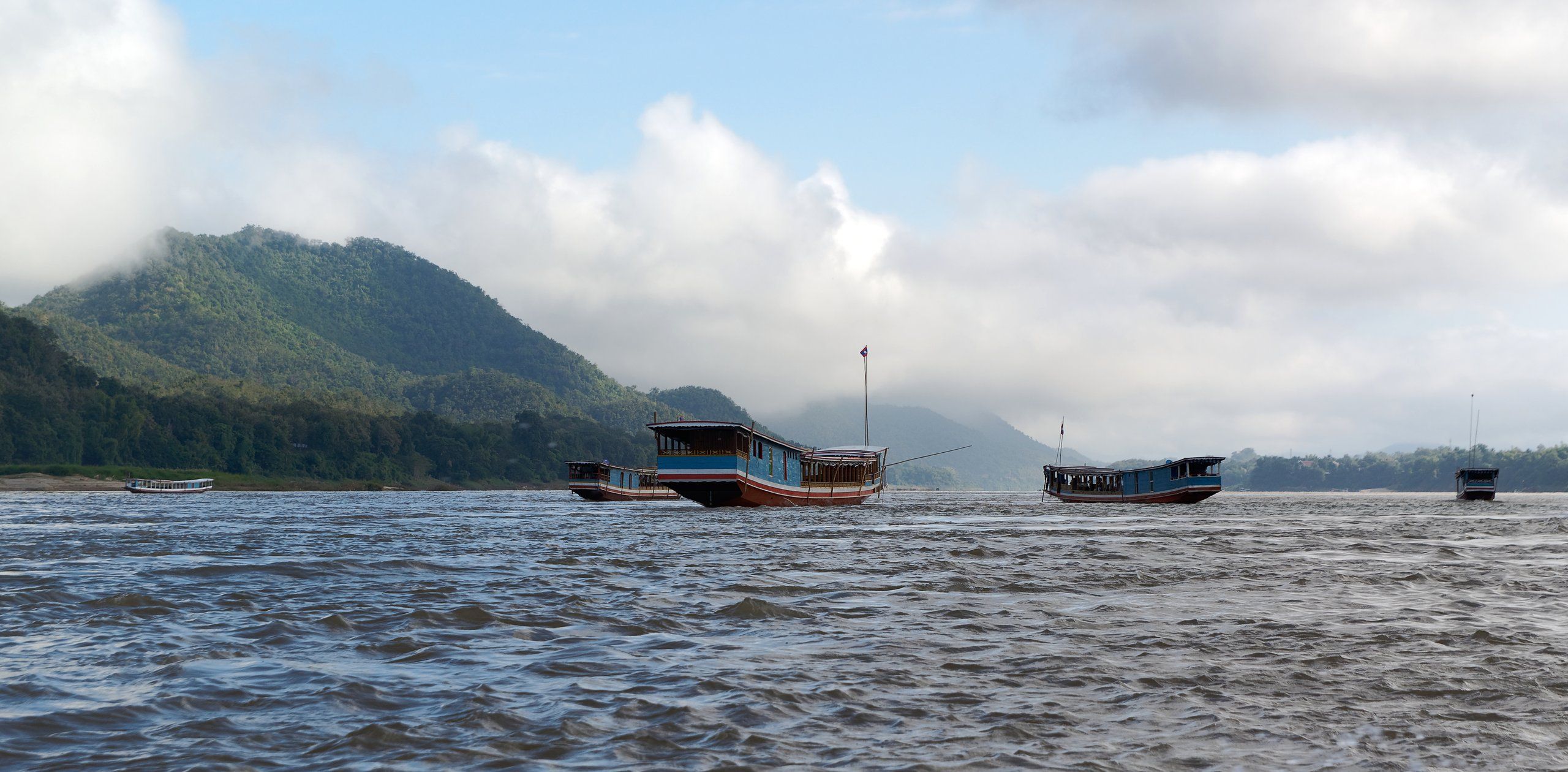 The Mekong at Luang Prabang, boats on choppy water below wooded hills and clouds