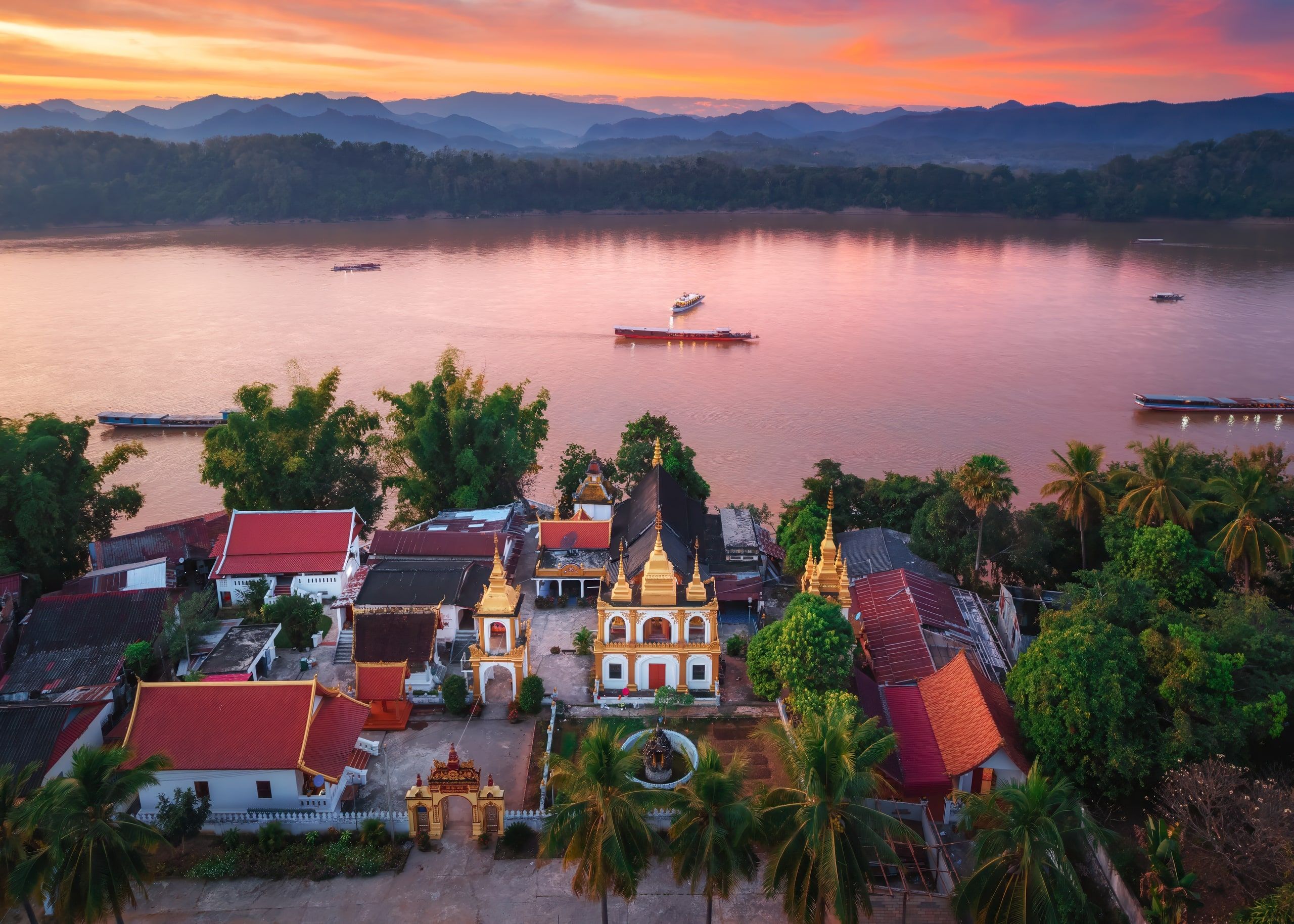 Luang Prabang vue du ciel au coucher du soleil, un temple aux toits dorés au premier plan et le Mékong derrière