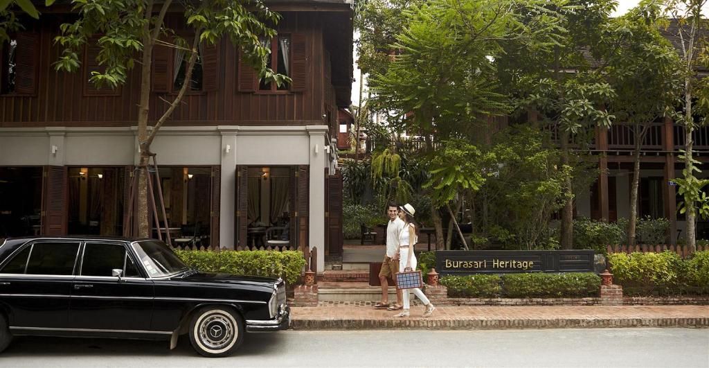La façade en bois du Burasari Heritage, avec son enseigne, derrière une haie, une voiture ancienne garée dans la rue