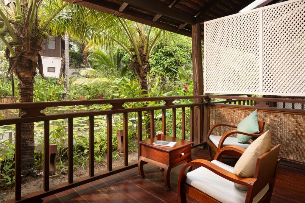 Une terrasse en bois de la Maison Dalabua, deux fauteuils face au jardin tropical et à un étang de lotus