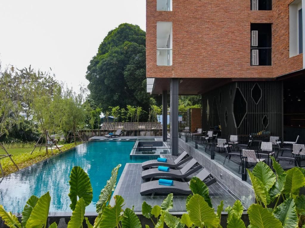 La piscine à débordement du VELA Dhi, ses transats et la façade de brique de l'hôtel