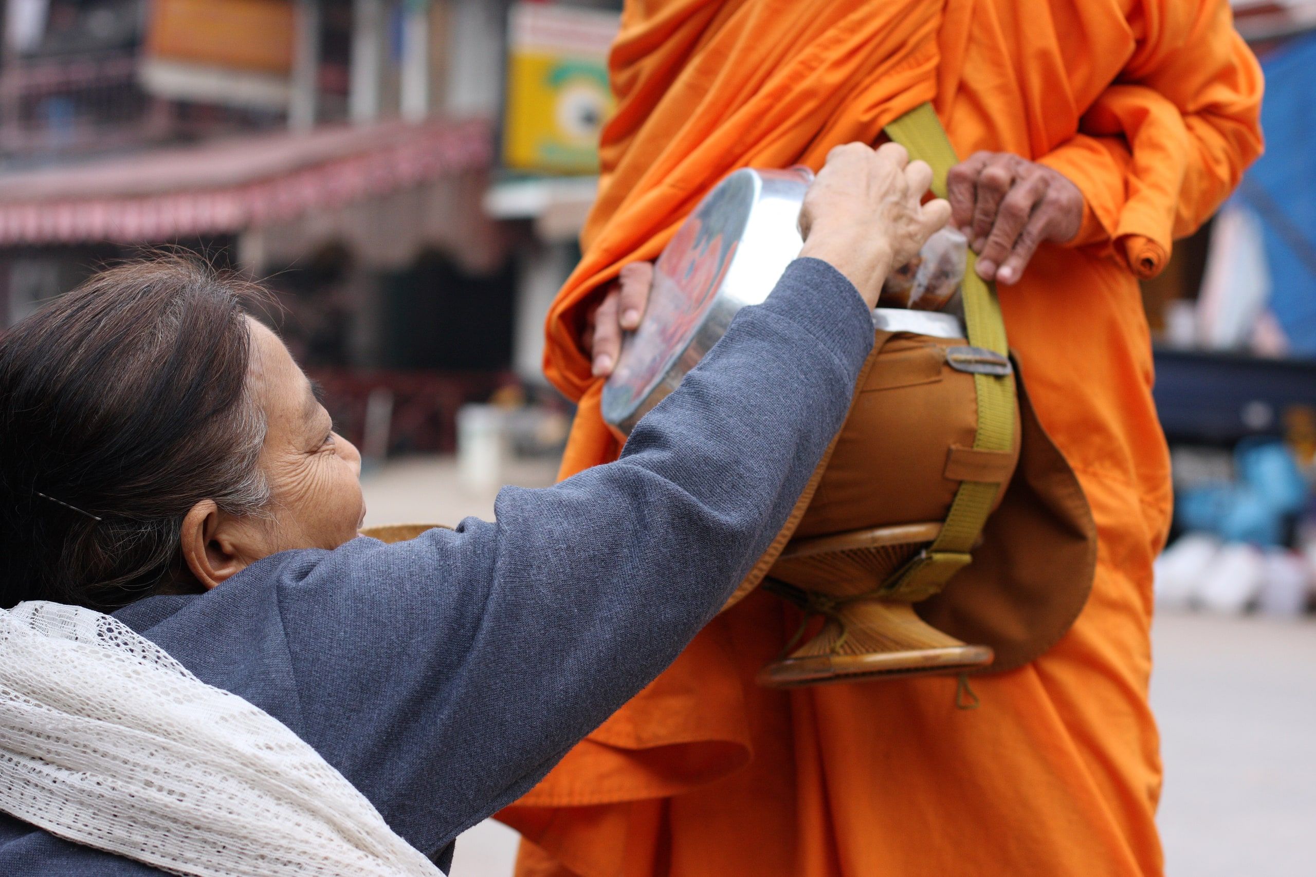 A woman places an offering in a monk's bowl in Pakbeng