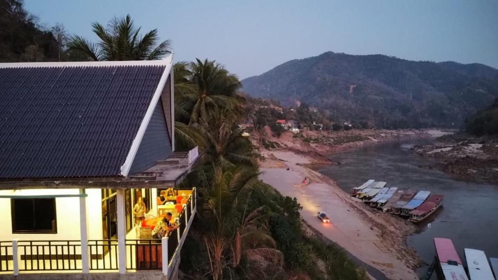 The lit terrace of Inn Riverside Hostel at dusk, above the slow boats moored on the Mekong bank