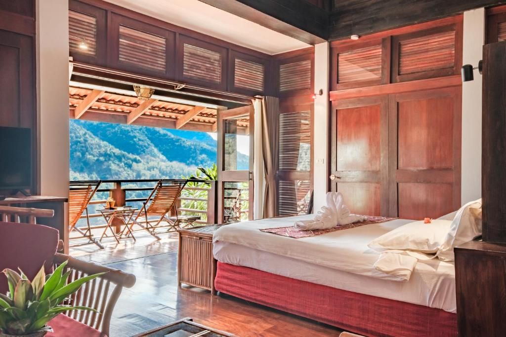 Une chambre en bois du Sanctuary Pakbeng Lodge, porte-fenêtre ouverte sur un balcon et des collines boisées