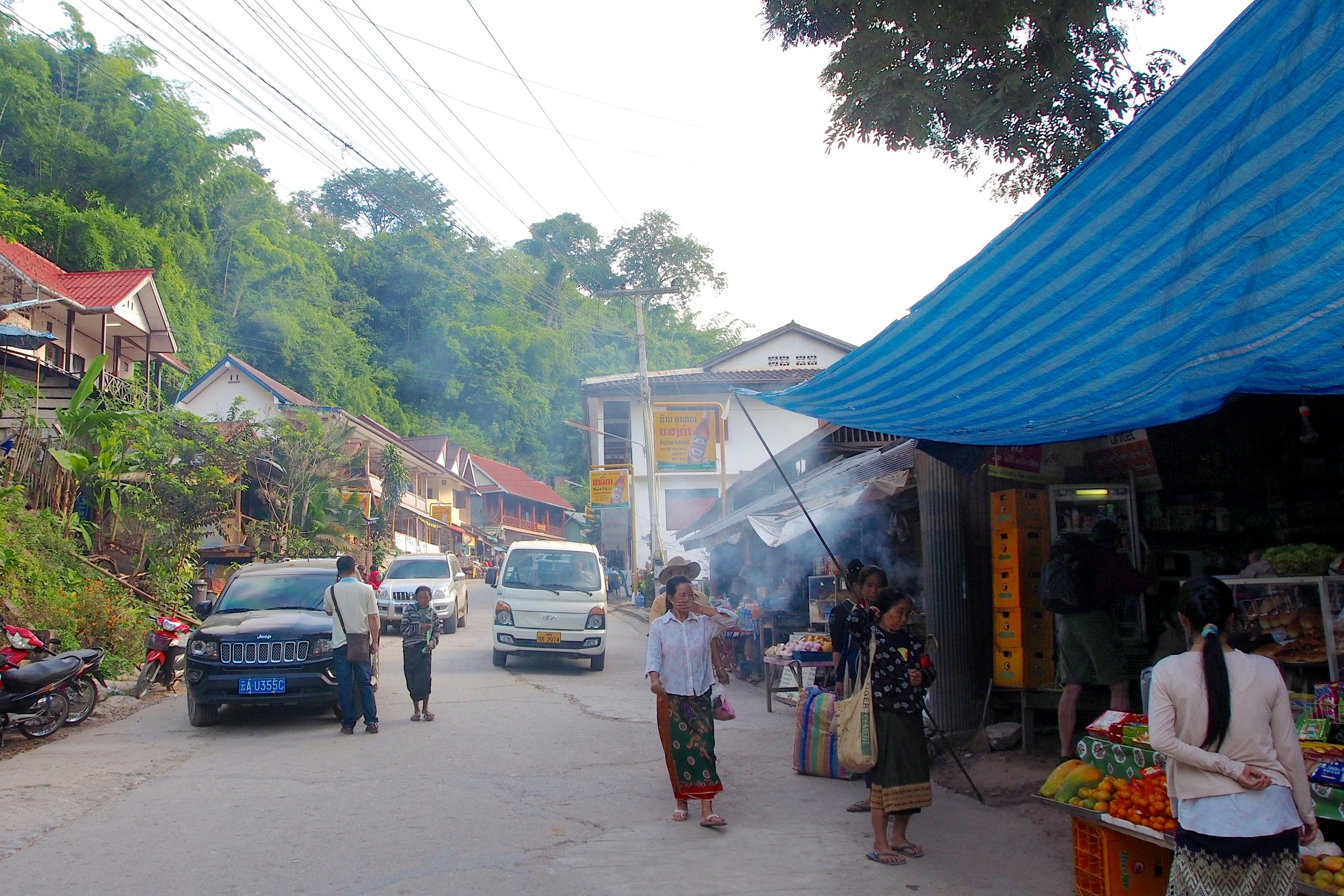 Stalls and passers-by on Pakbeng's main street below the wooded hills