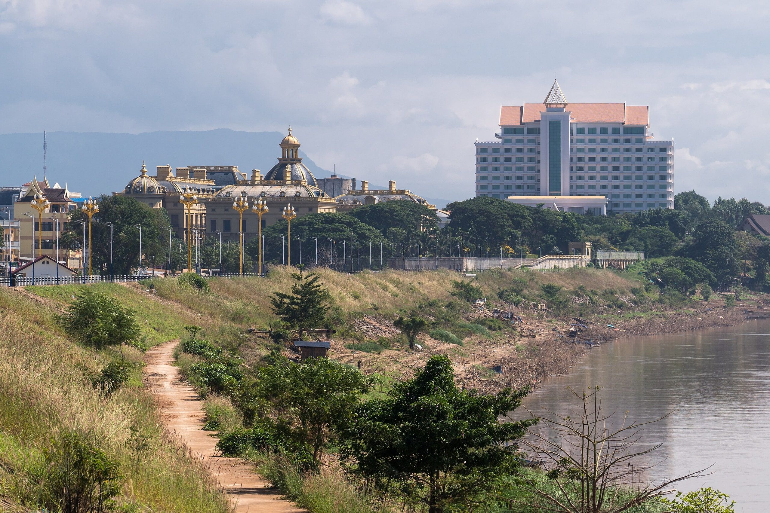 A path along the Mekong in Pakse, with a temple and a large hotel on the bank