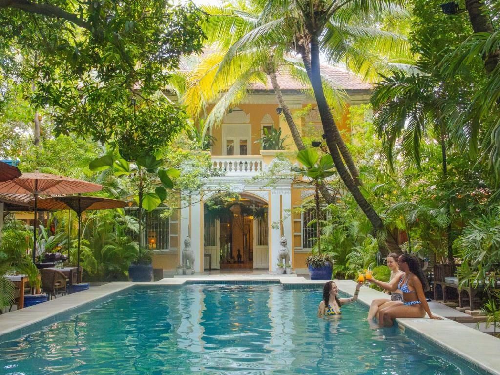 The Pavilion's pool in front of its yellow colonial villa, under palm trees