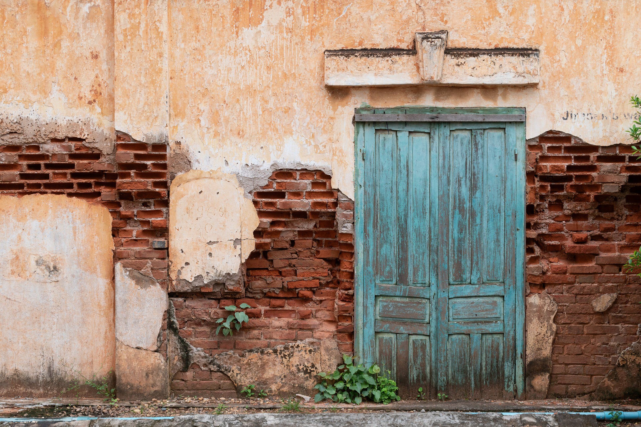 A blue wooden door in a crumbling wall of exposed brick, on Latsakhanai Road