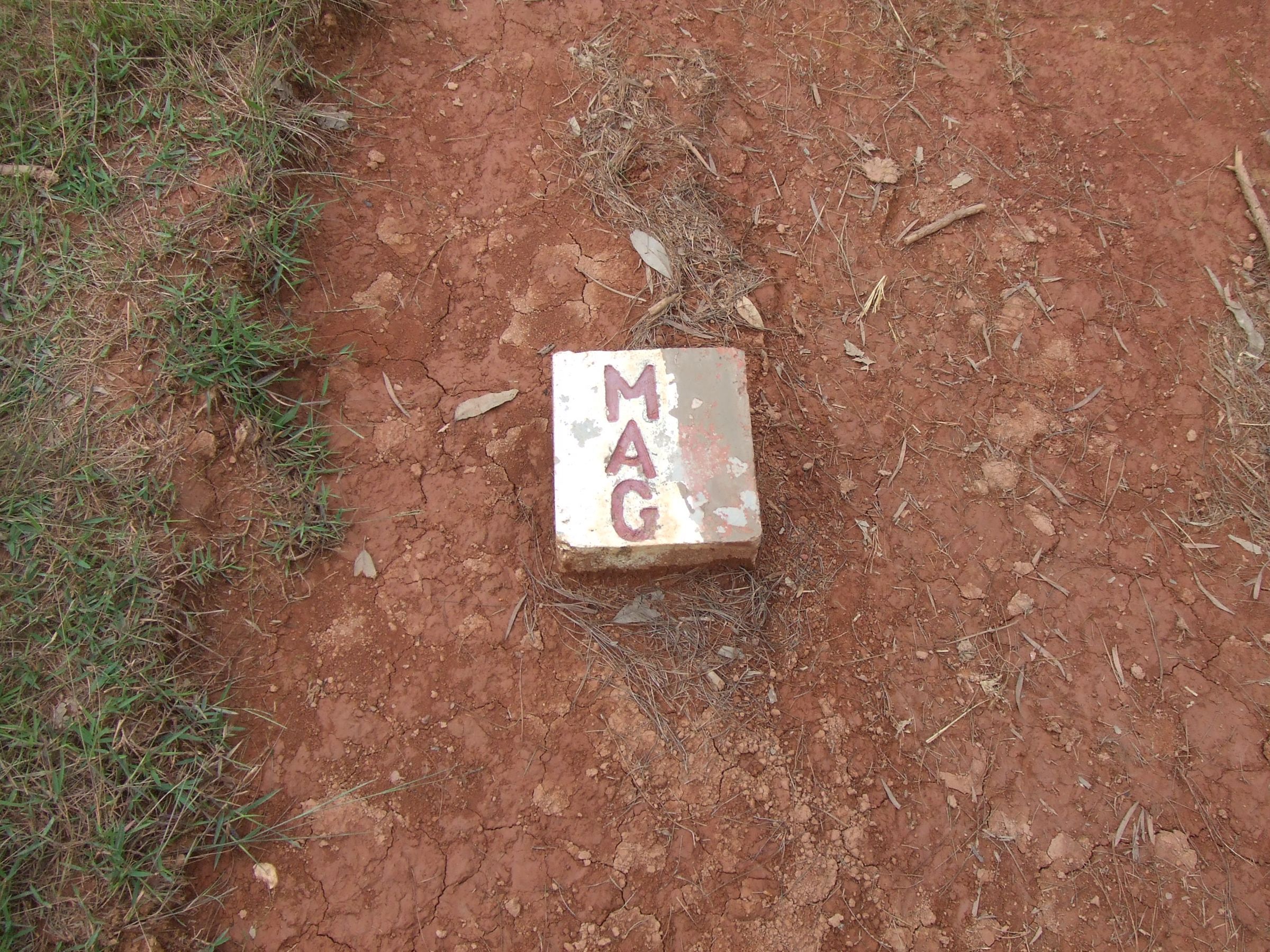 A concrete marker stamped MAG, set in red earth near Phonsavan by the demining organization