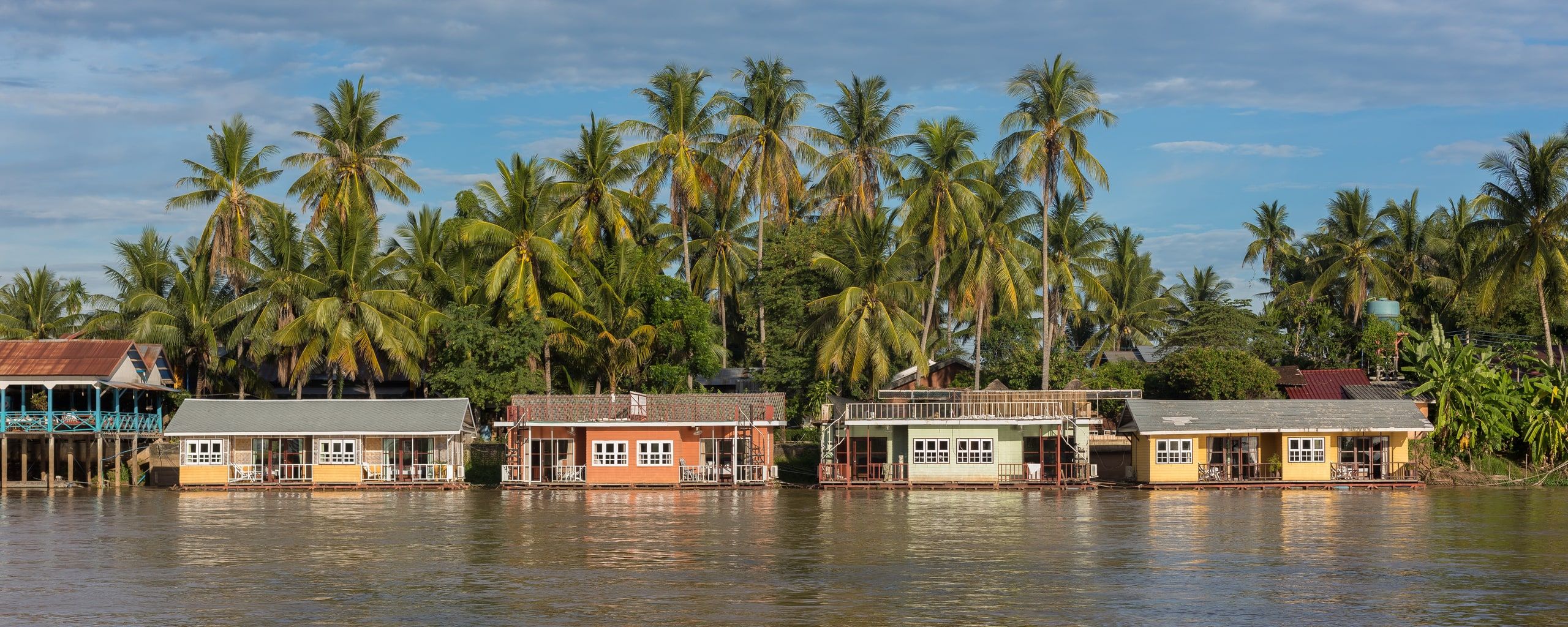 Colourful bungalows on the Mekong at Don Khon, under coconut palms