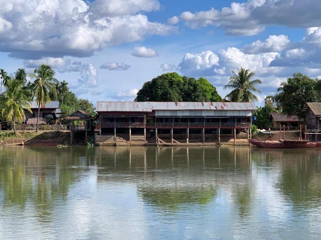 The long wooden house of Pa Kha Guesthouse by the river, under palm trees