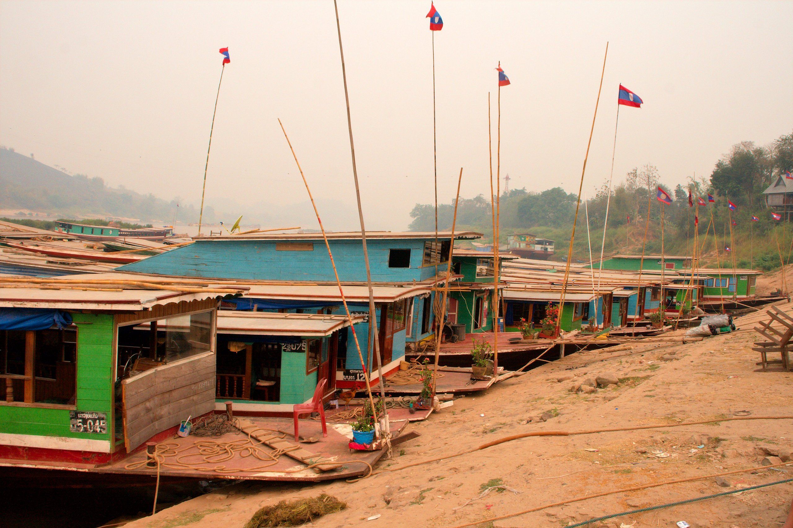 Des slow boats colorés amarrés au port de Huay Xai, au bord du Mékong, dans une lumière voilée