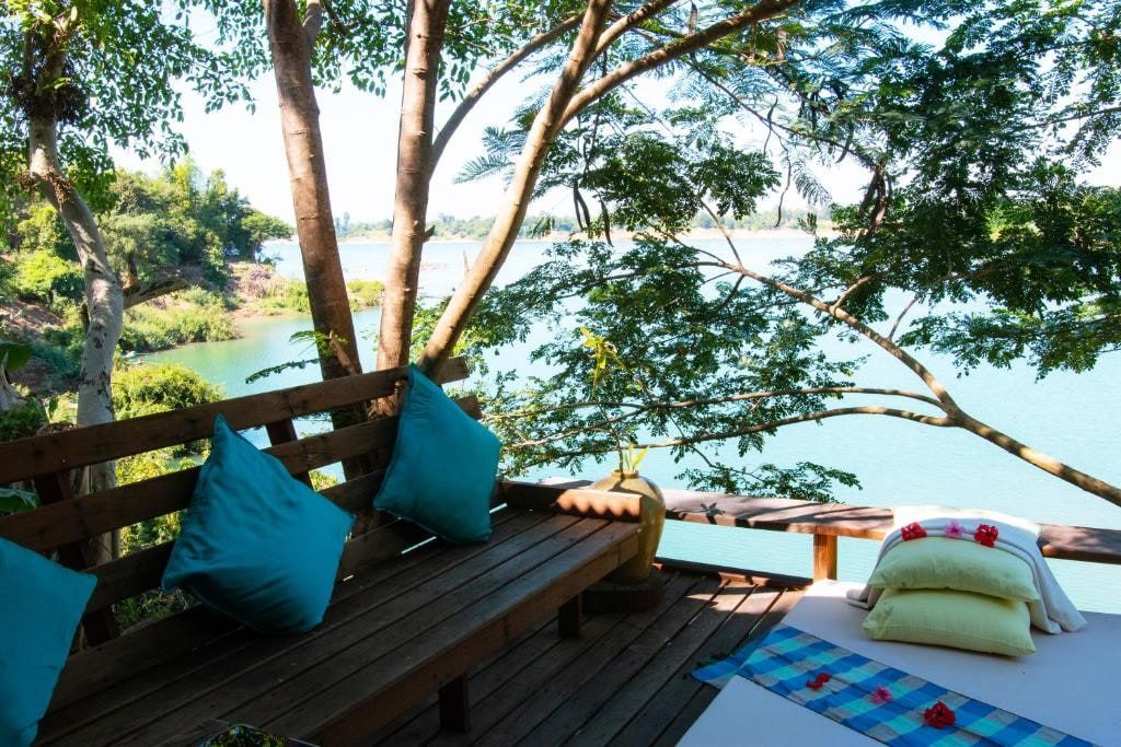Une terrasse de bois du Mekong Bird Resort, des coussins turquoise face au Mékong