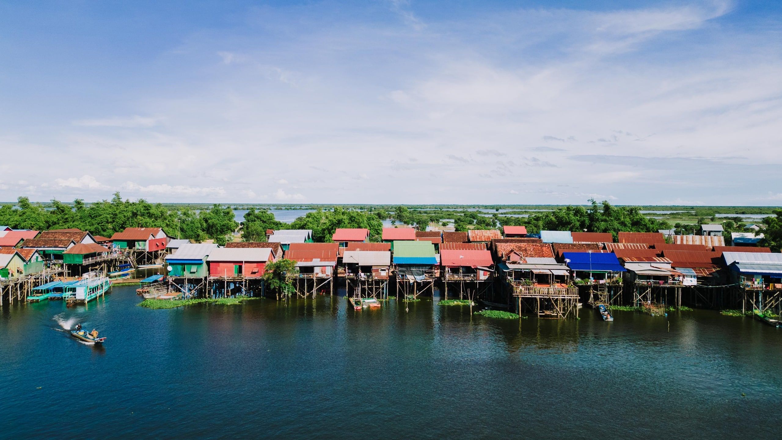 Stilt houses with colorful tin roofs along the water in Kampong Khleang, on the Tonle Sap, with a motorboat