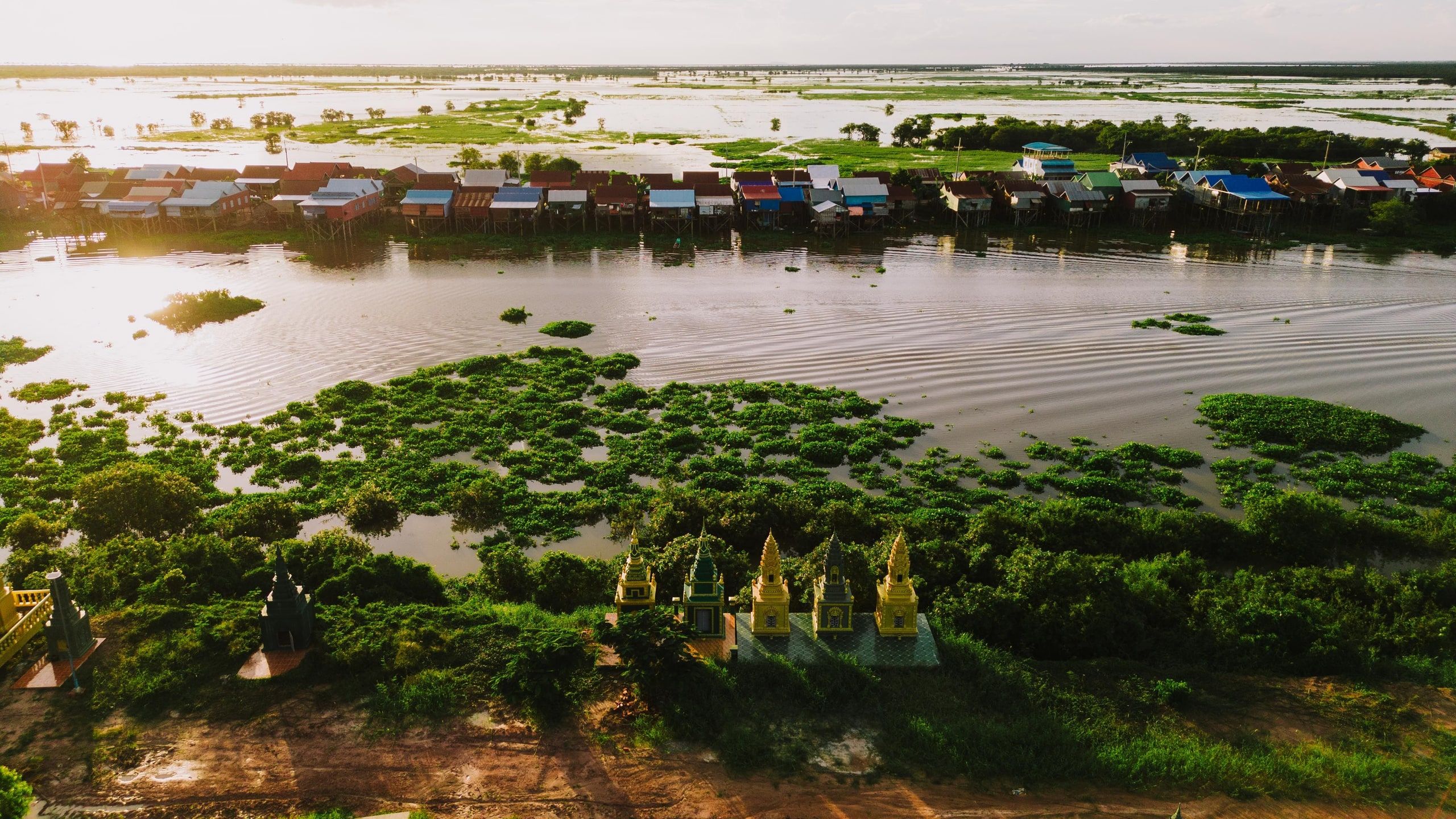 Kampong Khleang at sunset from the air: stilt houses along the water, flooded plains and golden stupas in the foreground