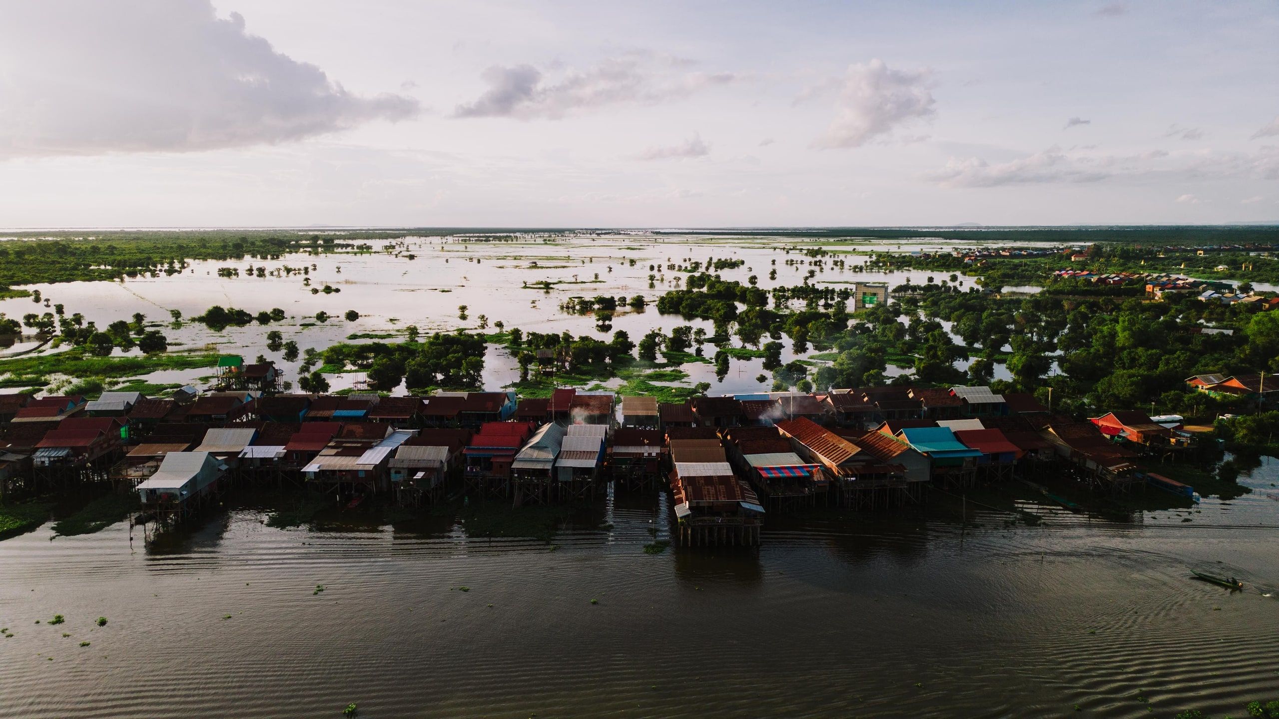 Aerial view of Kampong Khleang: a row of stilt houses in front of plains covered in water, dotted with trees